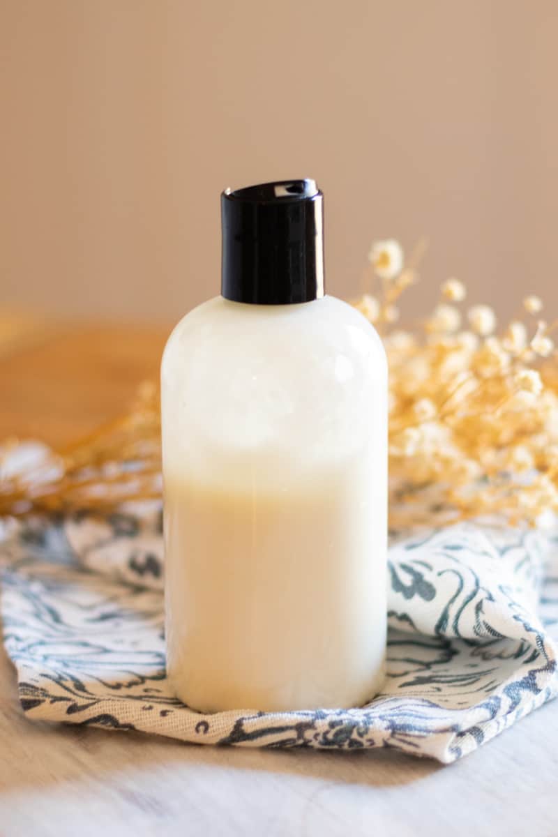 A homemade foot lotion in a plastic squeeze bottle sitting on a wooden table.