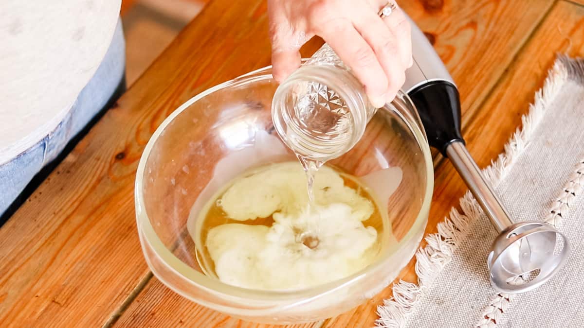 Pouring the distilled water into the bowl with the melted oils. 