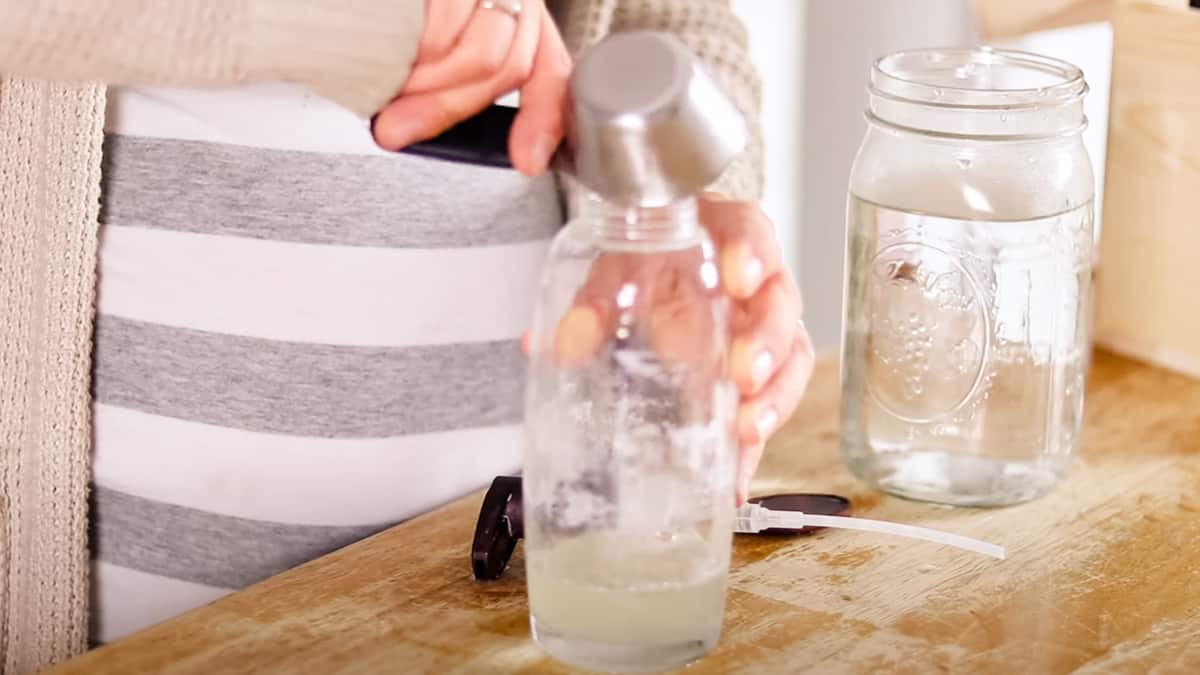 Using a measuring cup to add the liquid ingredients to the shampoo bottle. 
