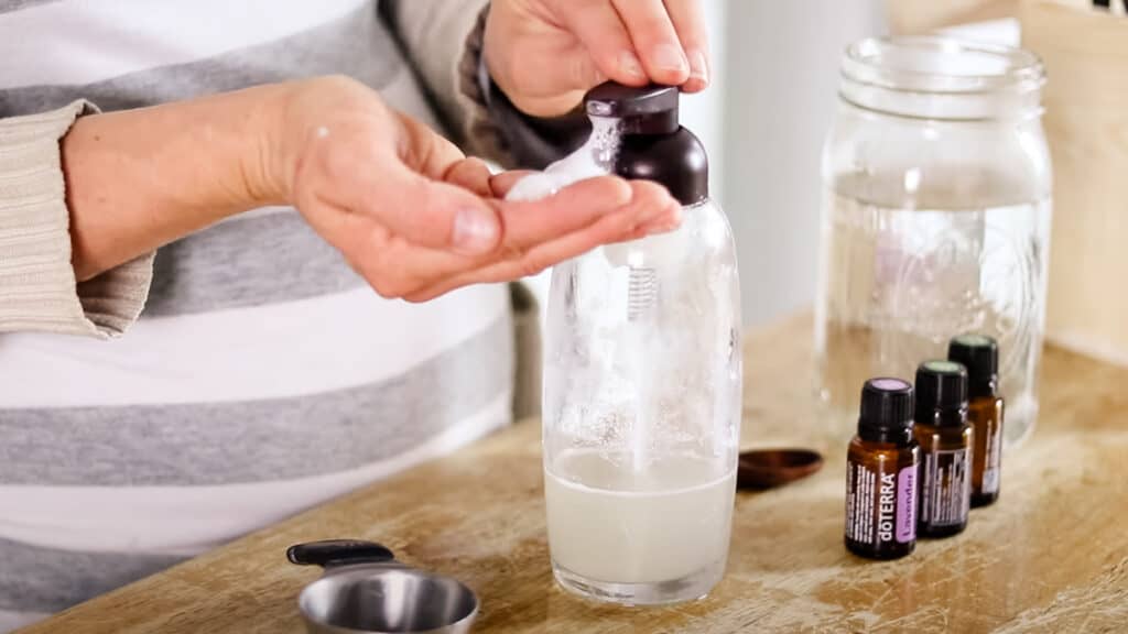 Dispensing homemade shampoo into the palm of my hand with the ingredients for this recipe on the table in the background.