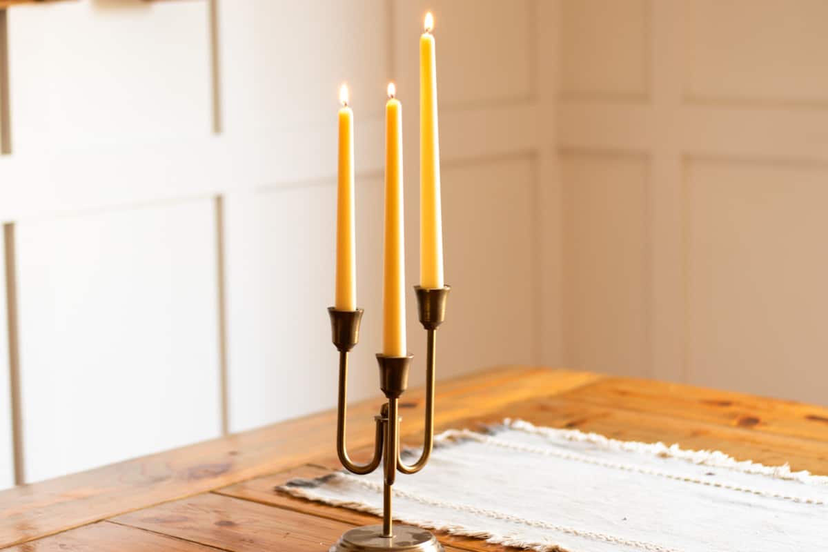 Taper candles burning in the corner of a room on a wooden table.