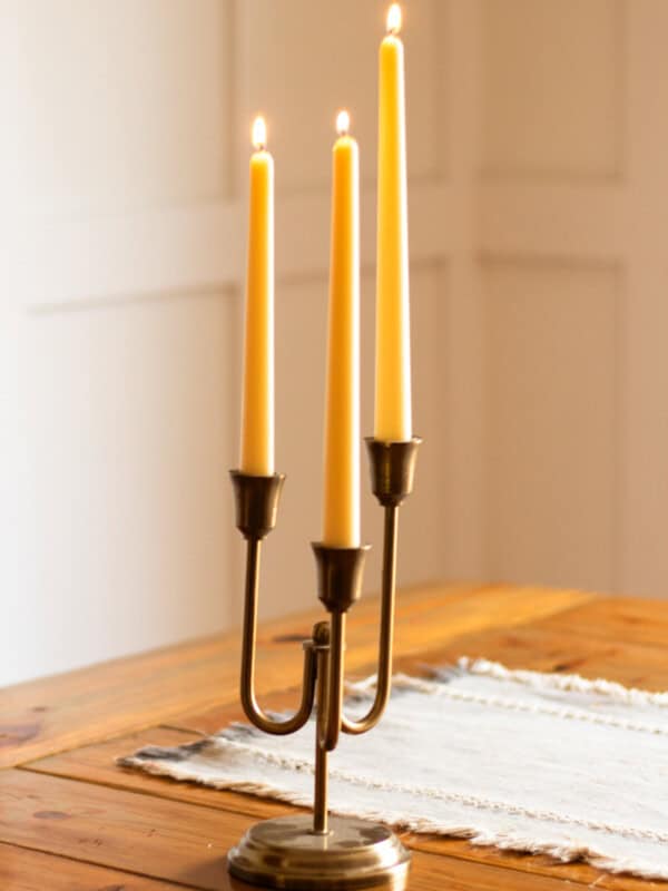 Taper beeswax candles burning brightly on a wooden table.