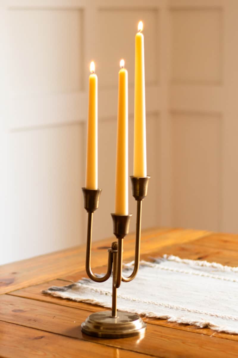 Taper beeswax candles burning brightly on a wooden table.