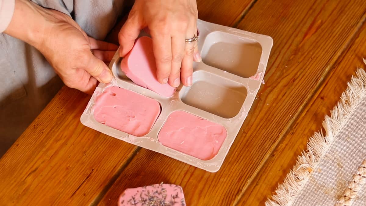 A woman removing pink homemade soap bars from a silicone mold.