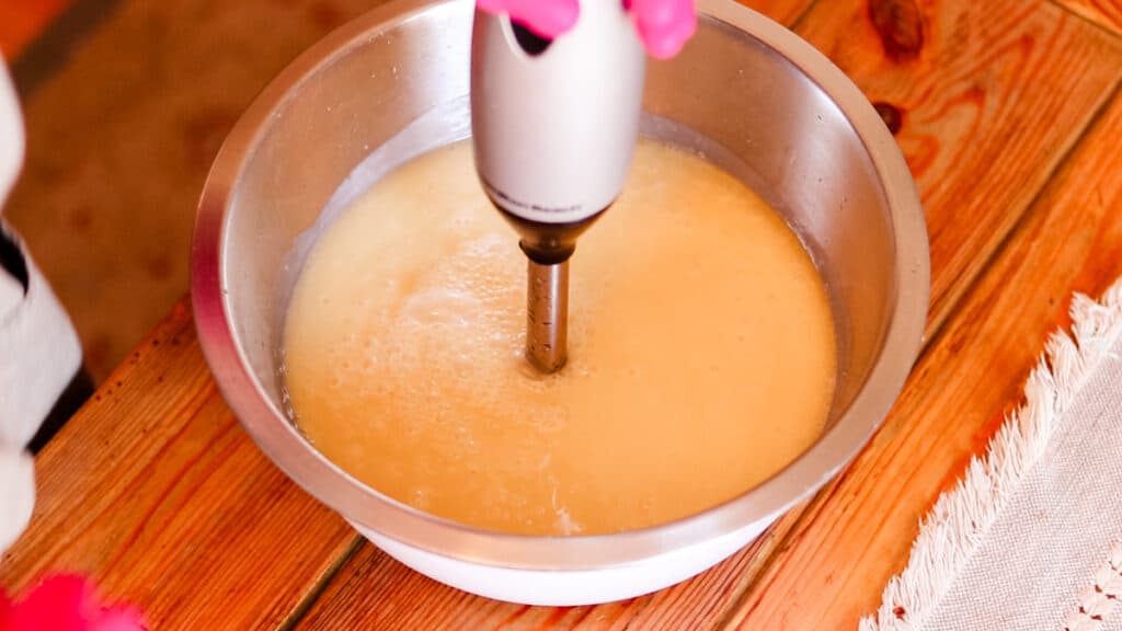 An immersion blender bringing a bowl filled with soap ingredients to a trace.