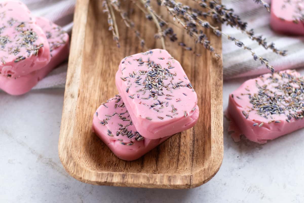 Homemade lavender soap bars with dried lavender buds curing on a wooden drying rack.