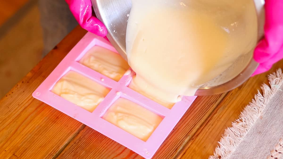 A woman pouring a bowl filled with soap batter into a silicone soap bar mold.
