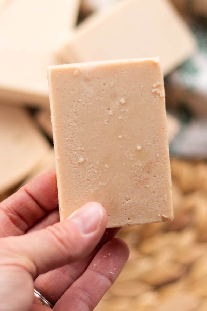A hand holding a bar of tan homemade cold process soap.