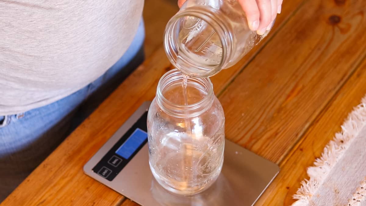 A woman pouring water into a glass mason jar that is on top of a digital scale.
