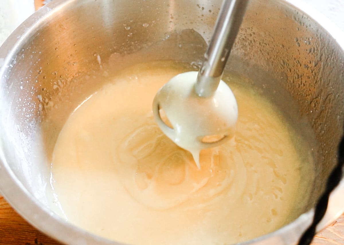 A stick blender held above soap in a large bowl filled with soap at a medium trace.