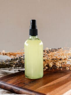 Whole body deodorant spray on a wooden tabletop with dried flowers in the background.