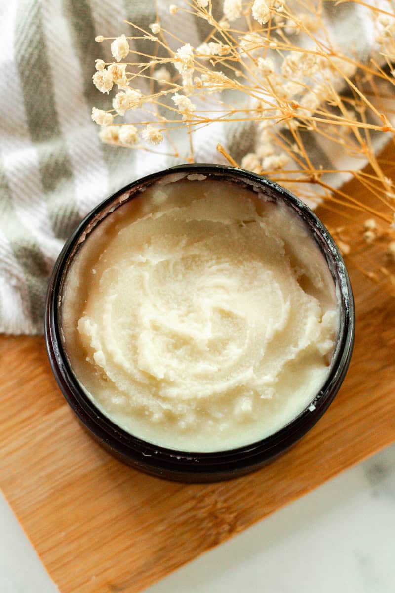 An amber jar of homemade deodorant cream sitting on a wooden board. 