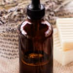 A DIY bath oil in an amber dropper bottle on a bath towel with white soap bars next to it.