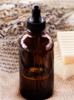 A DIY bath oil in an amber dropper bottle on a bath towel with white soap bars next to it.