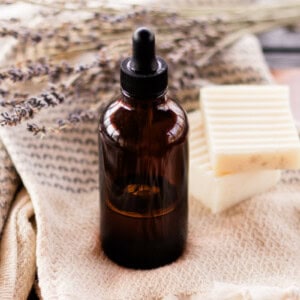 A homemade bath oil in an amber dropper bottle with a clean towel and textured soap bars next to it.