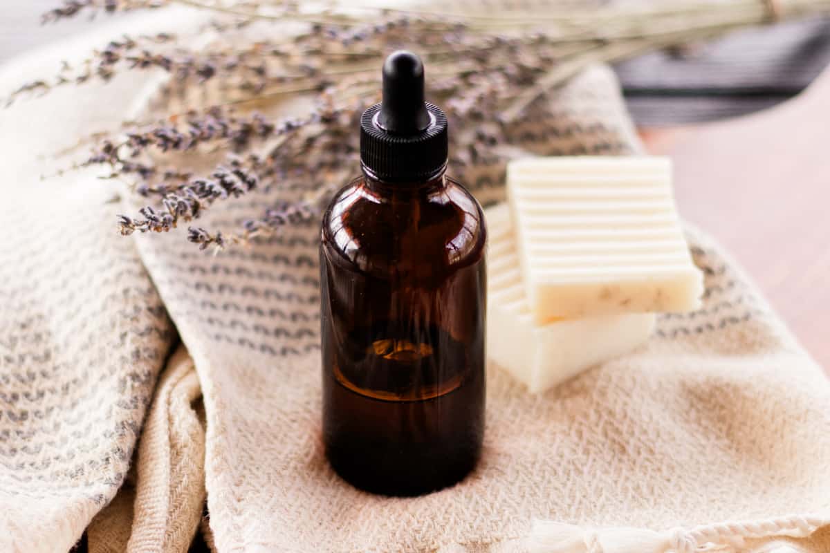 A homemade bath oil in an amber dropper bottle with a clean towel and textured soap bars next to it.