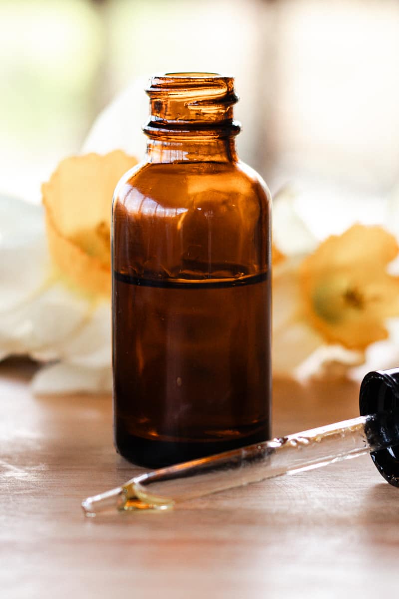 Bottle of scalp serum on a wooden table with a dropper top next to it.