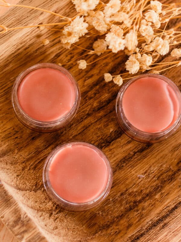 3 tinted lip balm tubes with flowers in the background.