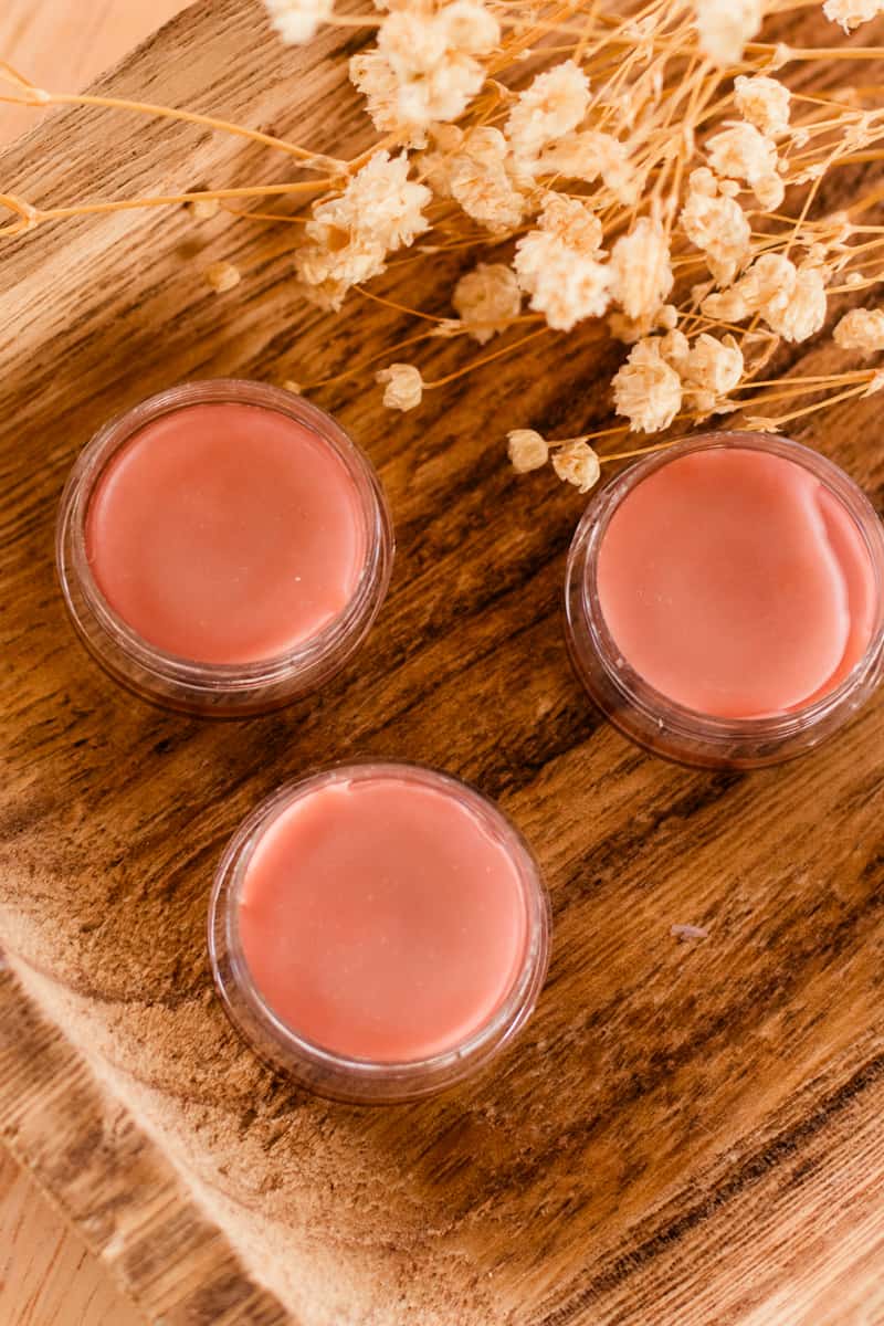 3 tinted lip balm tubes with flowers in the background.