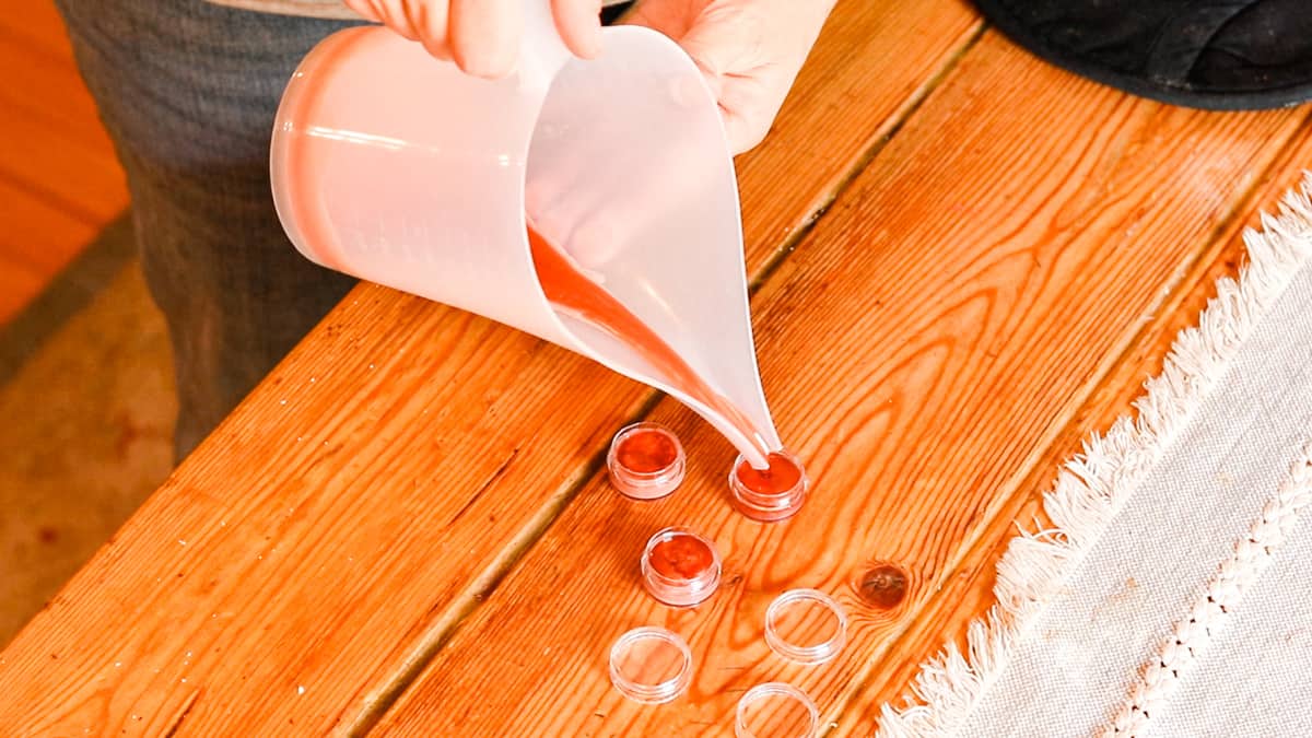 Pouring the tinted lip balm mixture into lip balm containers.