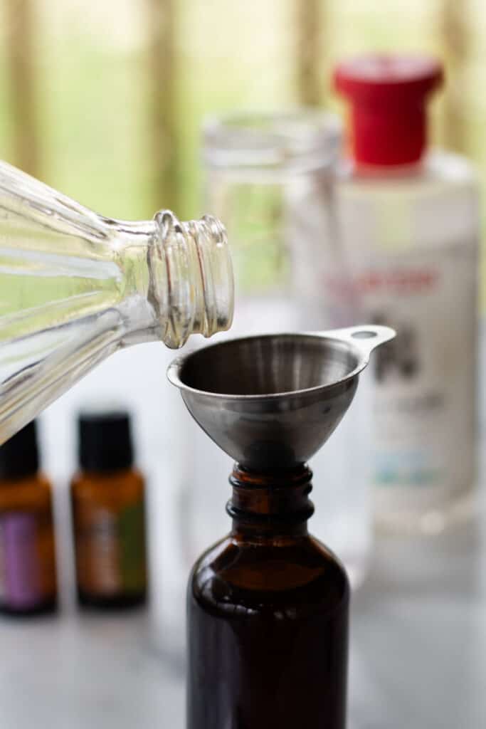 Pouring the apple cider vinegar into the bottle using the metal funnel.