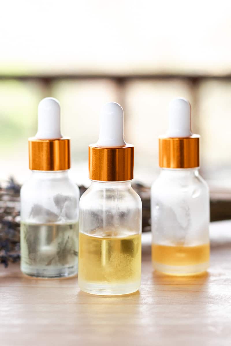 Three glass bottles with copper lids and droppers that hold various DIY facial serums for youthful skin.
