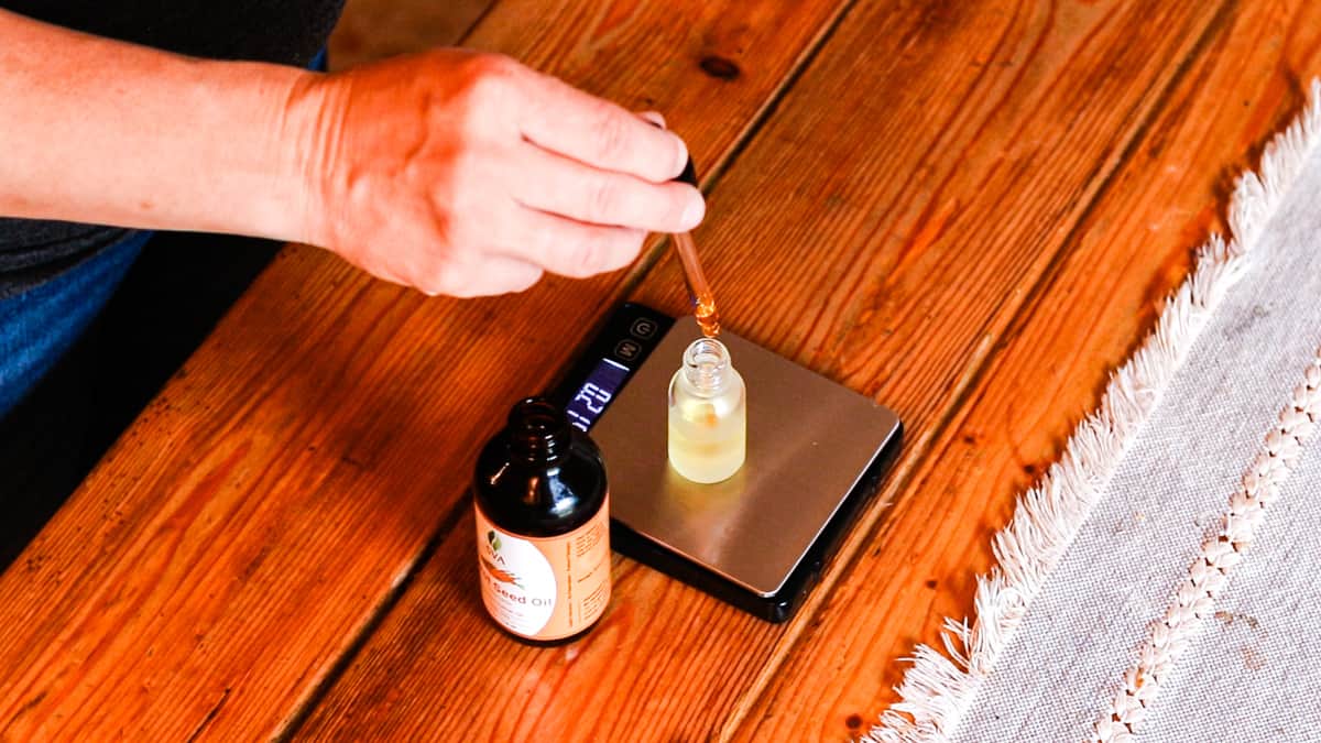 Glass bottle on a digital scale with carrot seed oil being dropped in it to make an anti-aging face serum.