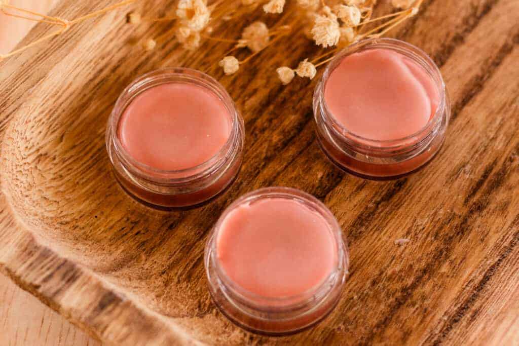 Three containers of tinted lip balm with the lids off.