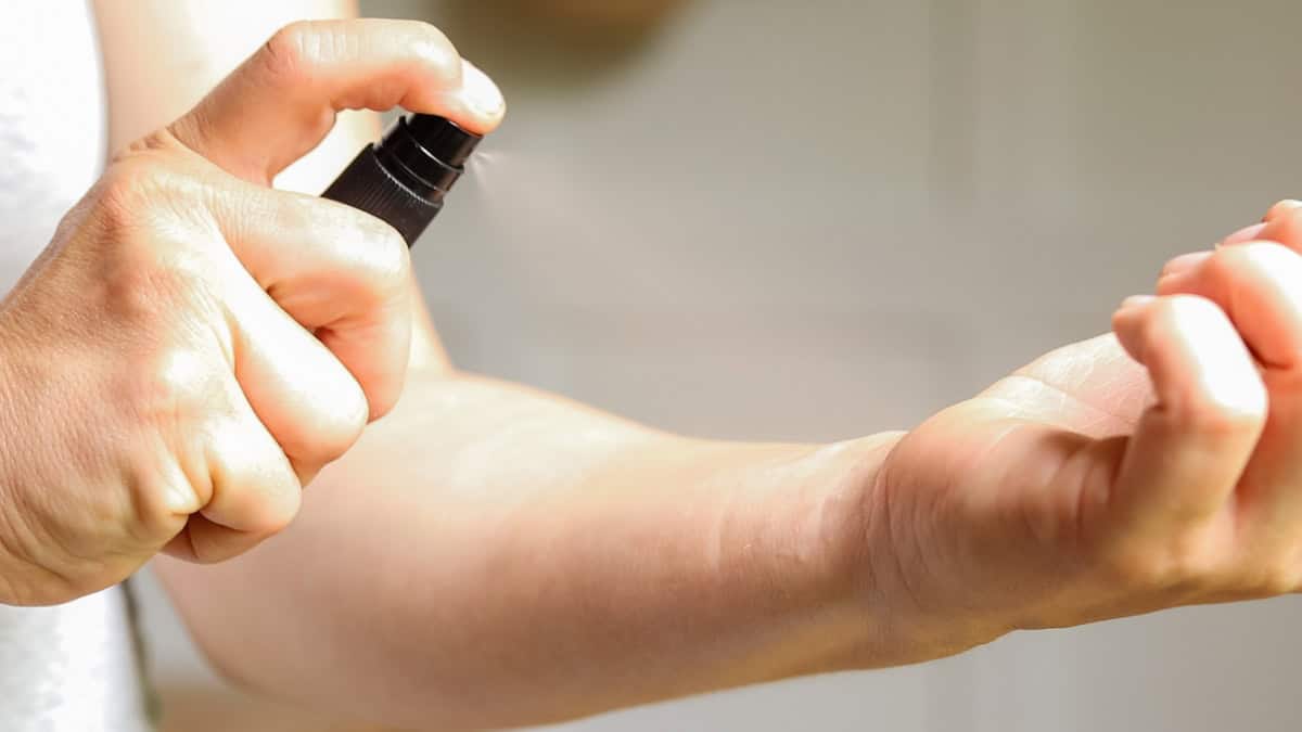 One hand pumps the black lid of a perfume spray bottle to spray the opposite wrist.