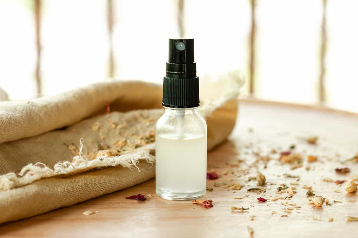 Ylang ylang spray perfume in a clear bottle with dried flowers and a decorative towel next to it.
