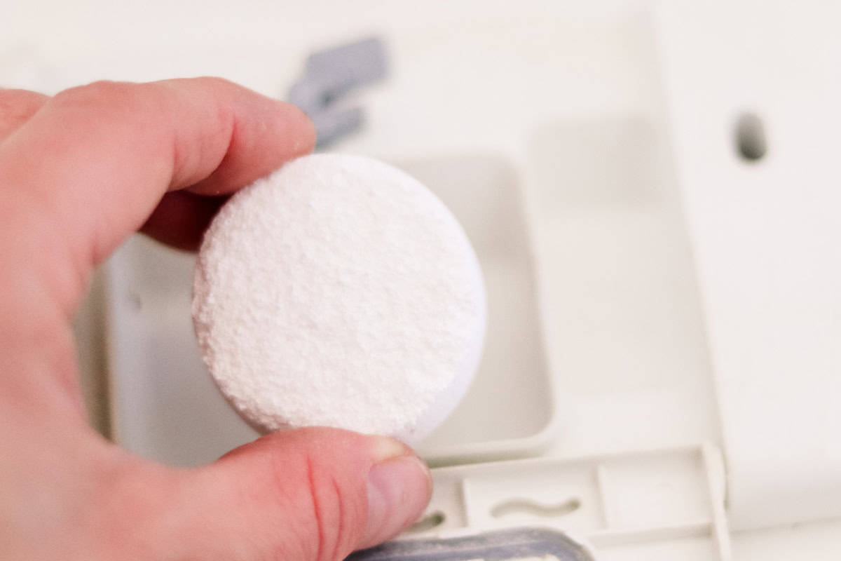 Placing a homemade dishwasher soap tab into the soap compartment.