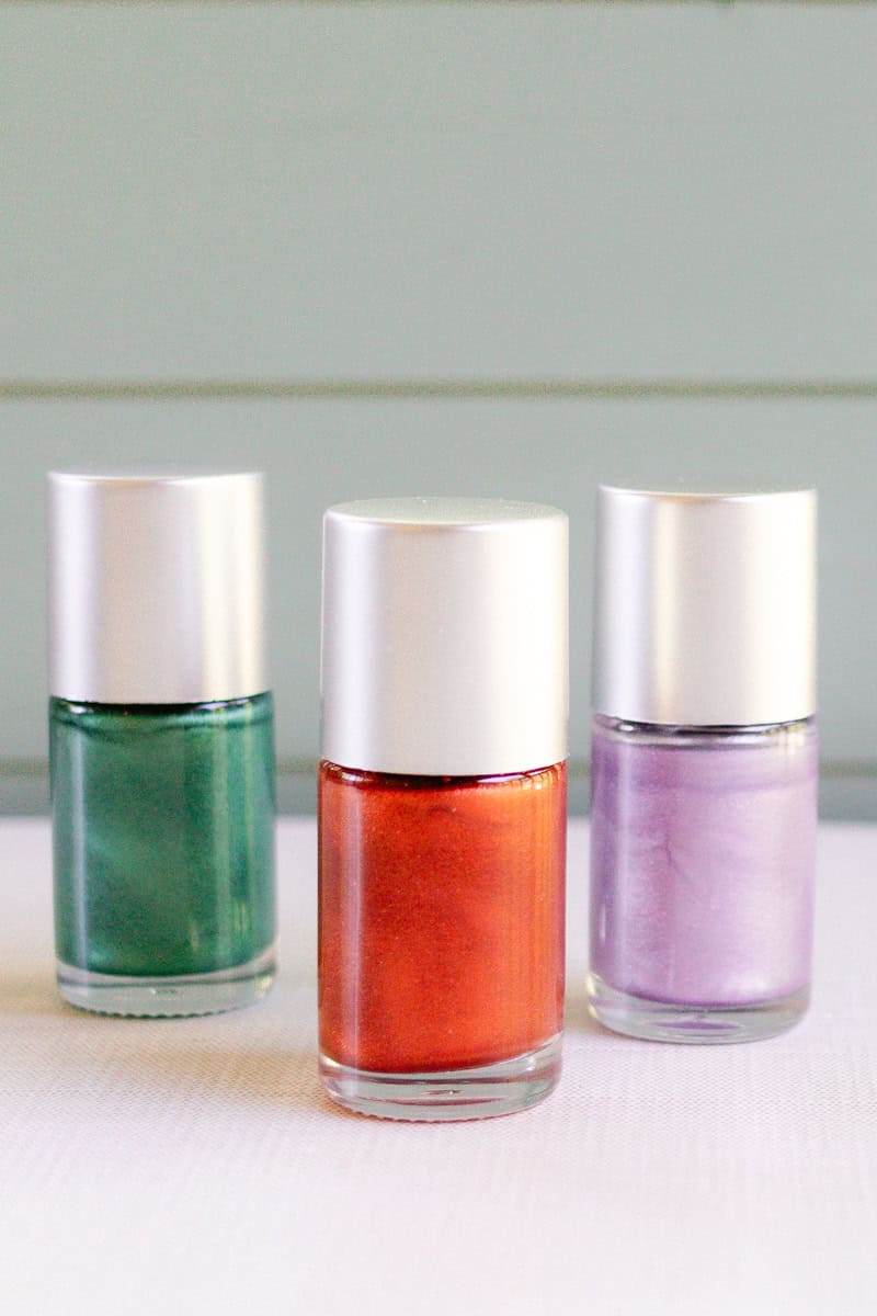 Three bottles of homemade nail polishes lined up on a counter. They are colored green, red, and purple. 