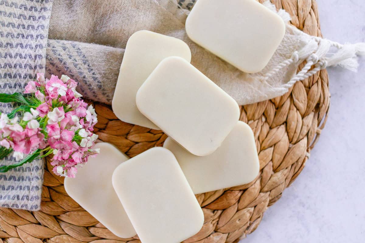 Soap bars for the face on a wicker mat with purple flowers next to it.