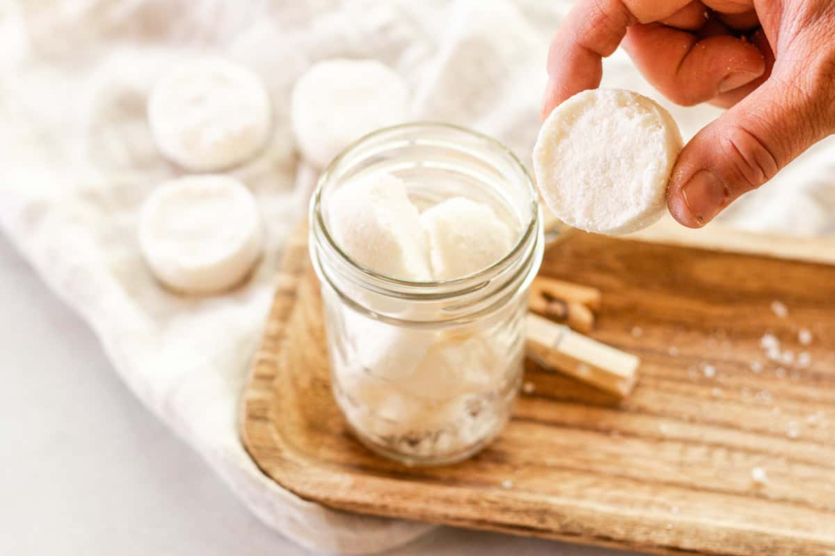 Holding a DIY laundry soap pod up with a jar of soap pods in the background. 