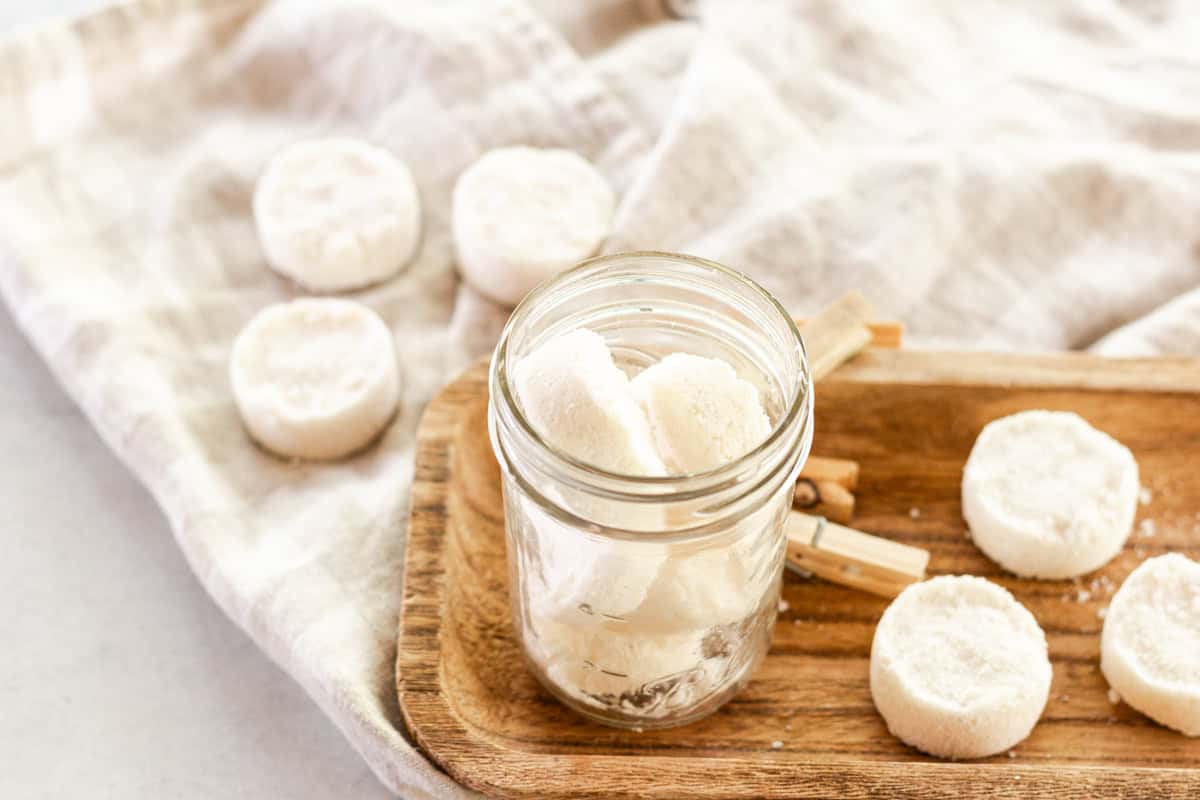 A mason jar with laundry soap pods in it and laundry soap pods scattered around the jar with clothespins.