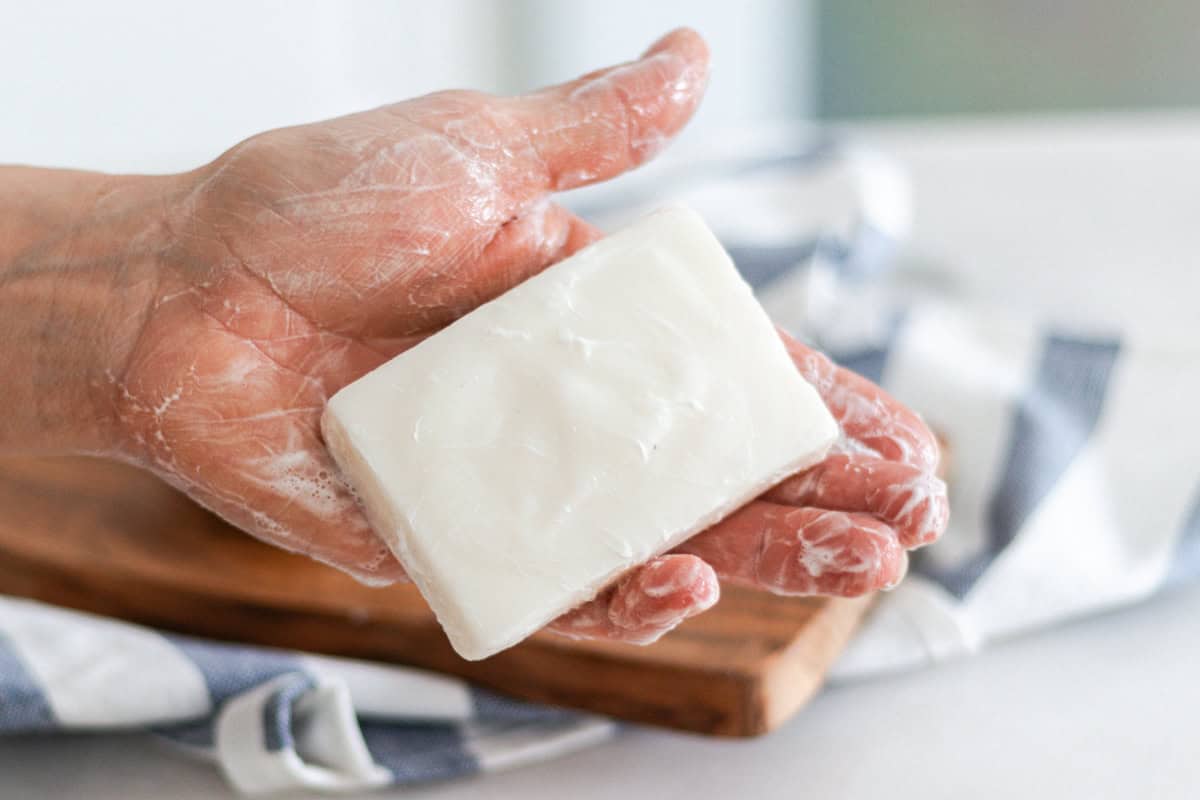 A hand holding a bar of cold process tallow soap.