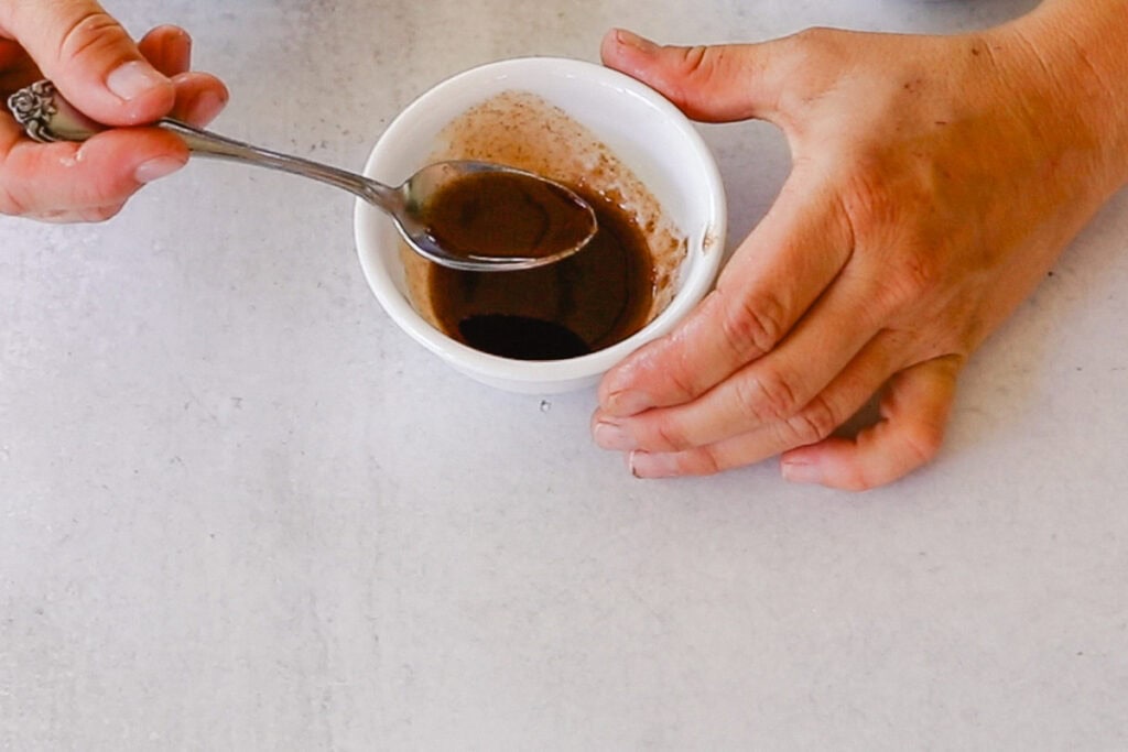 Stirring a bowl of exfoliating lip plumper with brown sugar. 