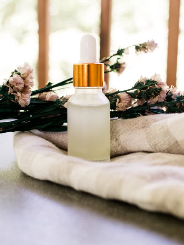 DIY eye serum in a clear dropper bottle with decorative flowers and a white and brown checker tea towel.