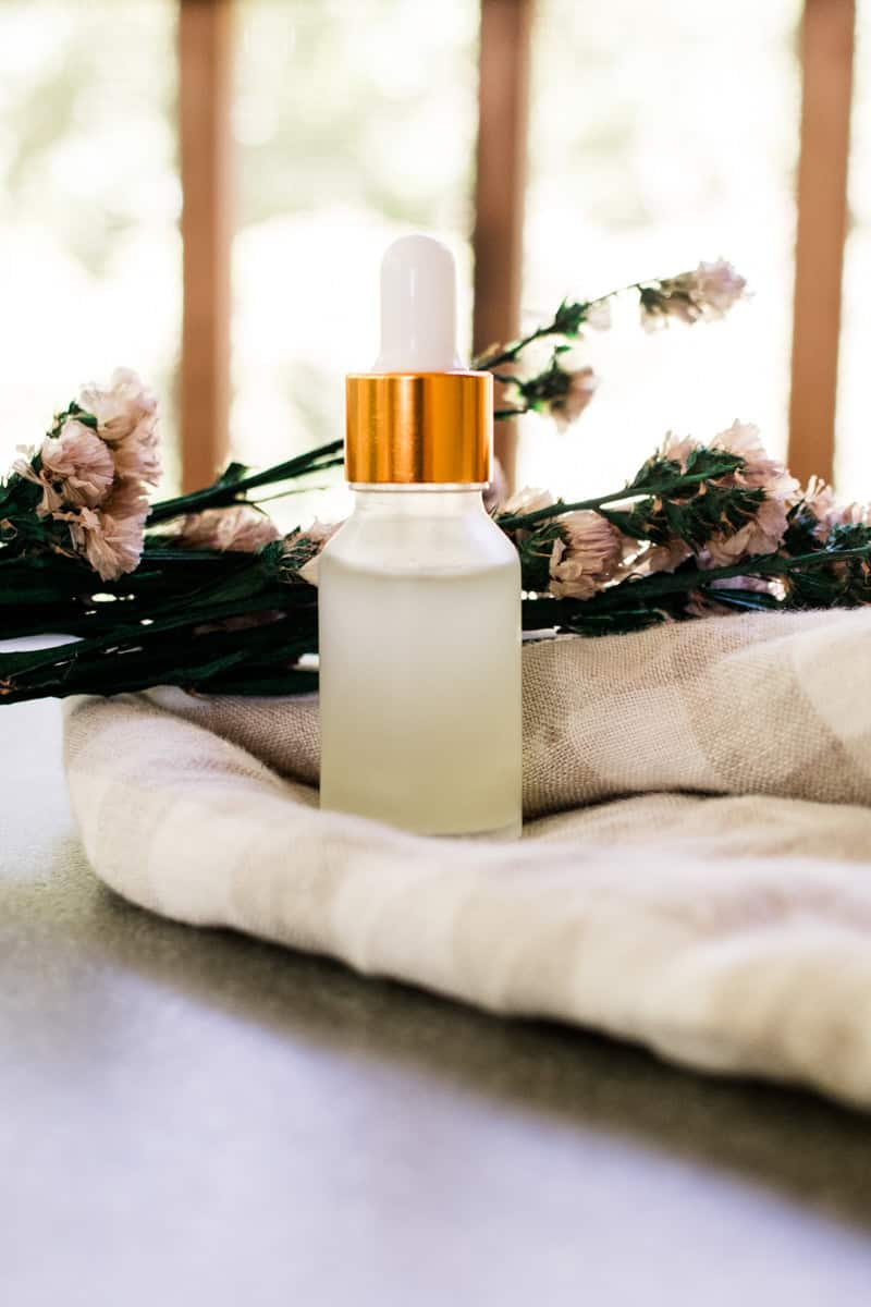 DIY eye serum in a clear dropper bottle with decorative flowers and a white and brown checker tea towel.