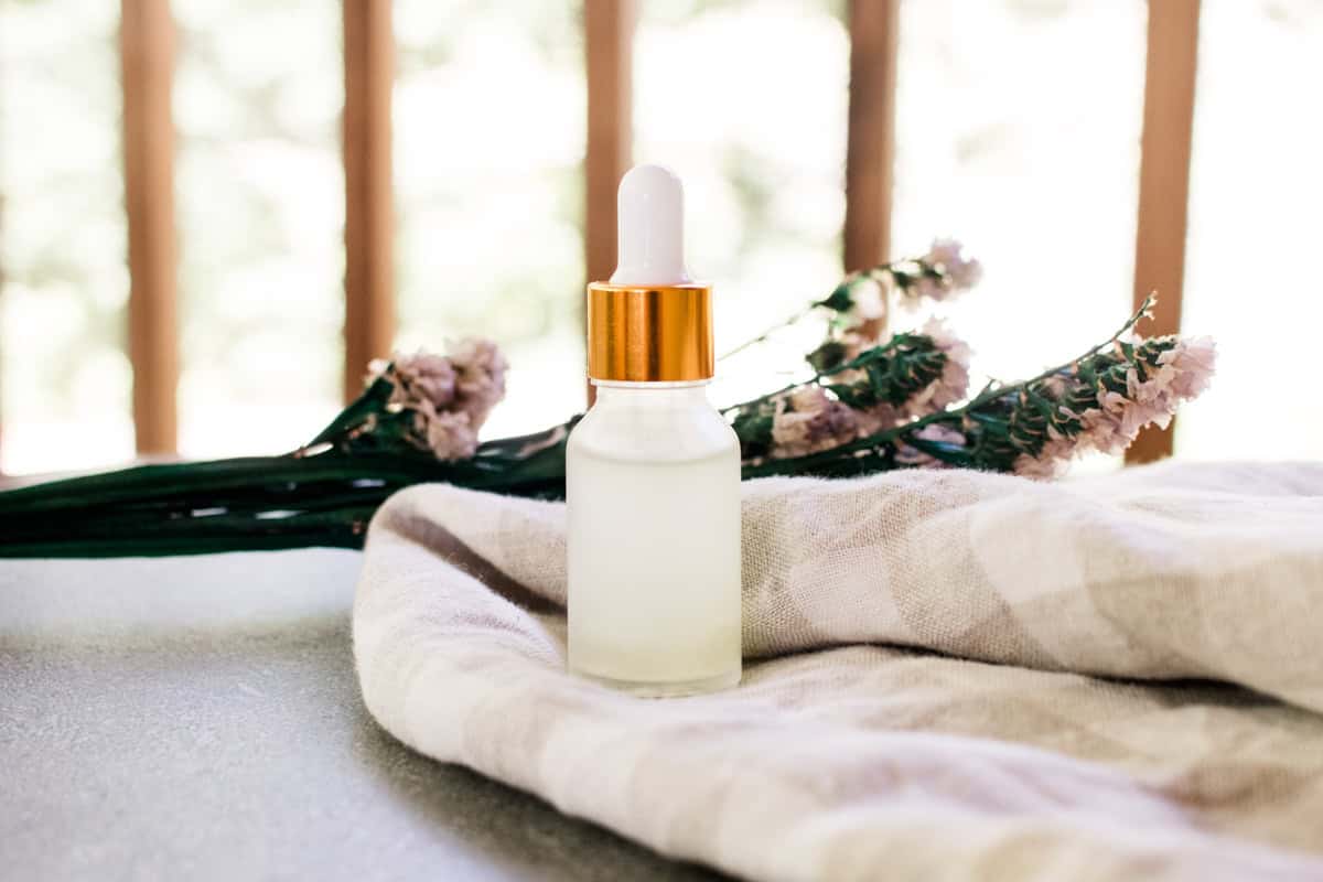 A glass dropper bottle of homemade eye serum on a linen towel with dried flowers in the background. 