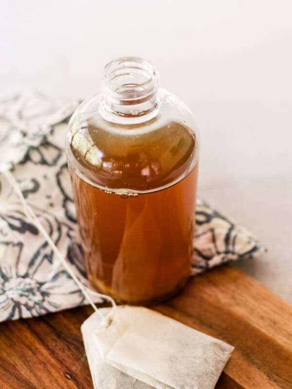 A bottle of green tea toner with a tea bag on a wooden board.