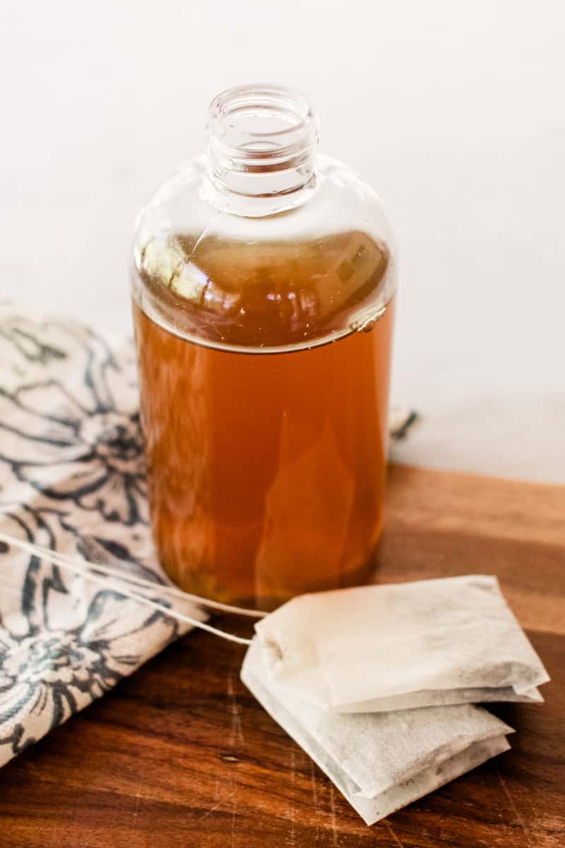 A clear glass bottle with homemade green tea toner in it sitting next to some tea bags. 