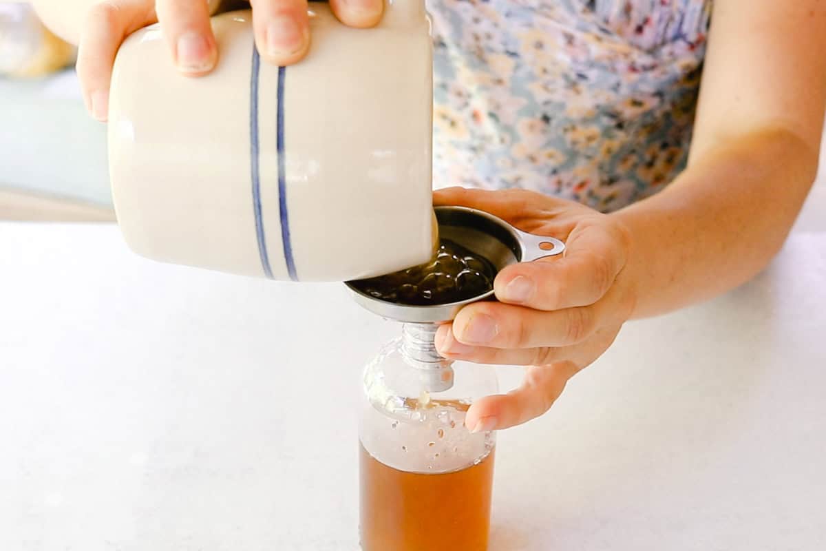 Pouring tea into a glass bottle with a funnel.