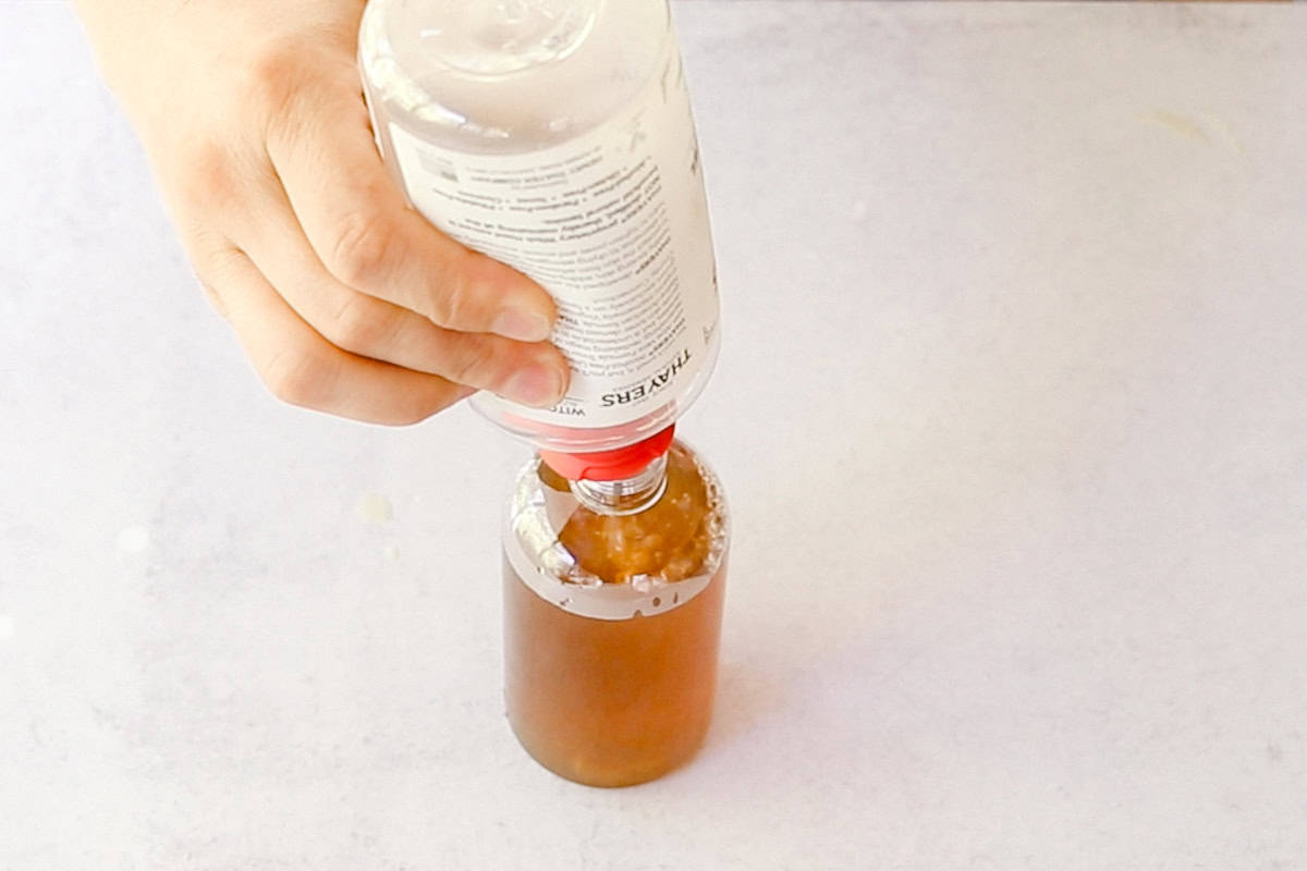 Pouring witch hazel into a bottle of tea.