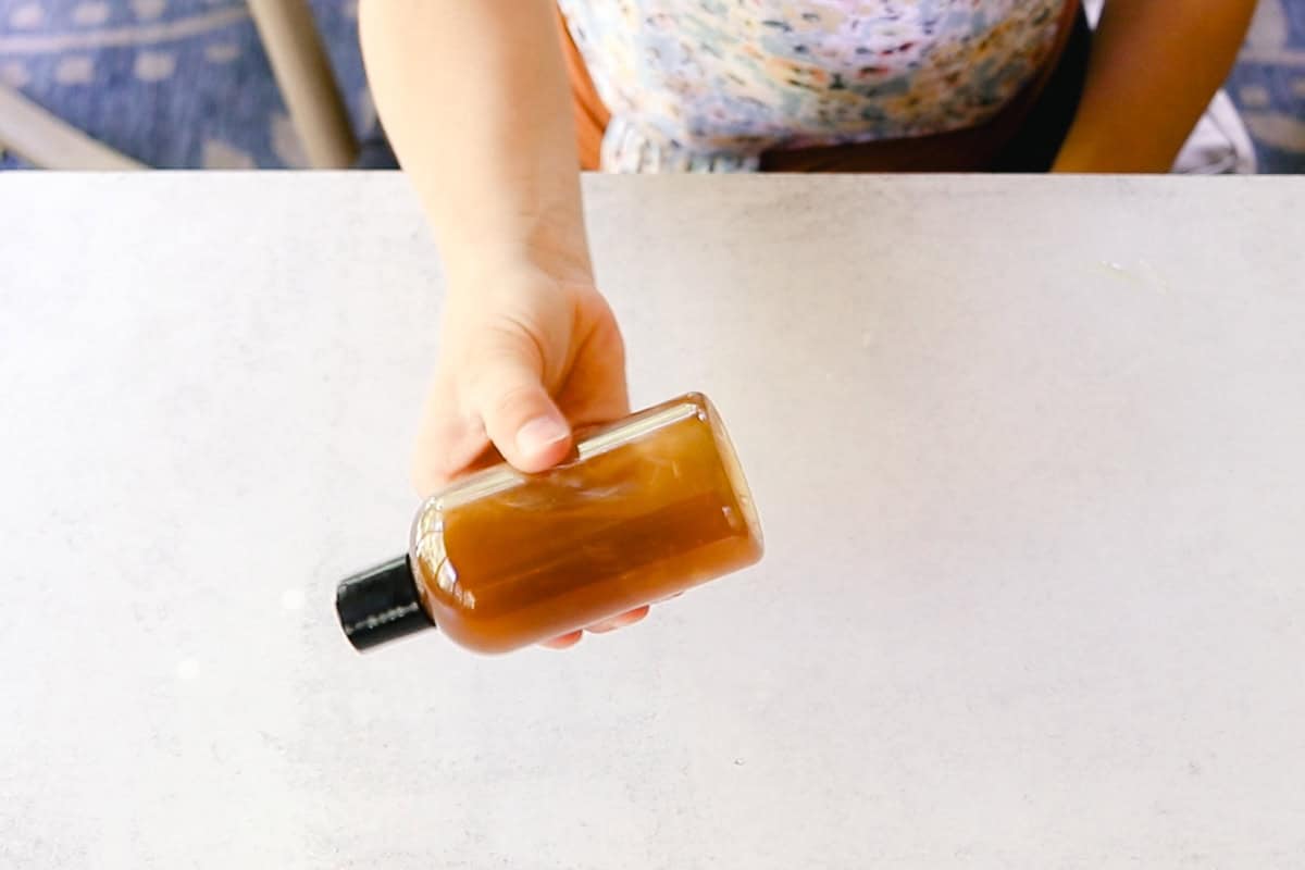 Holding a bottle of green tea toner over a white countertop. 