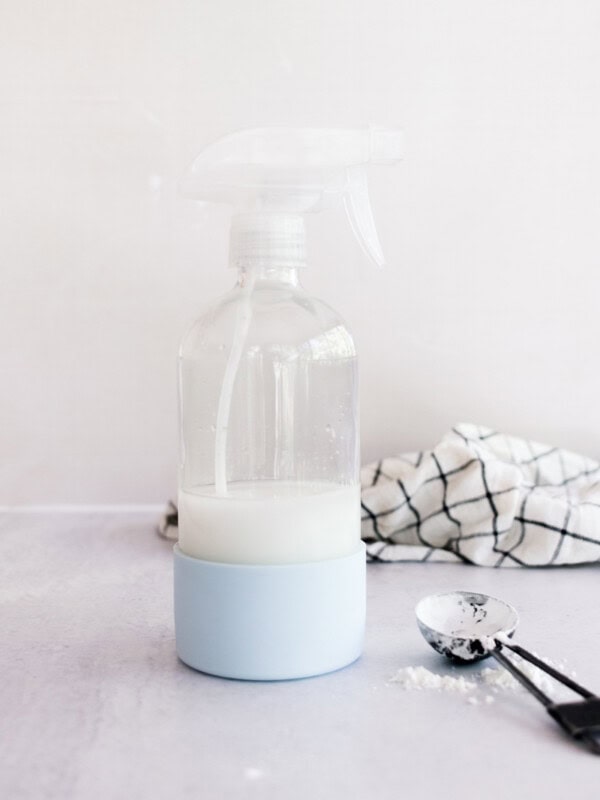Homemade spray starch in a glass spray bottle on a white marble laundry table.