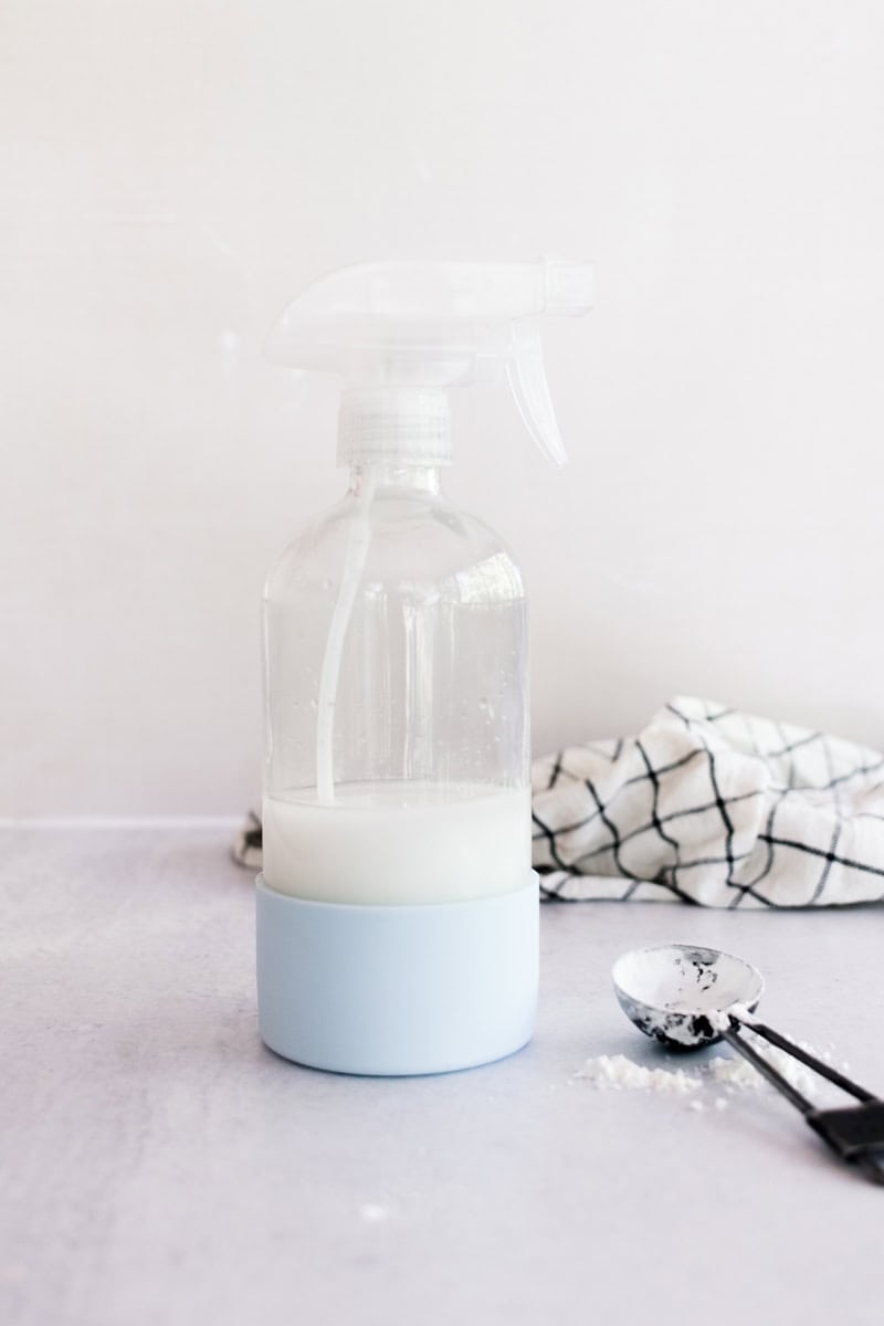 A bottle of spray starch with a tablespoon of cornstarch and a towel in the background. 