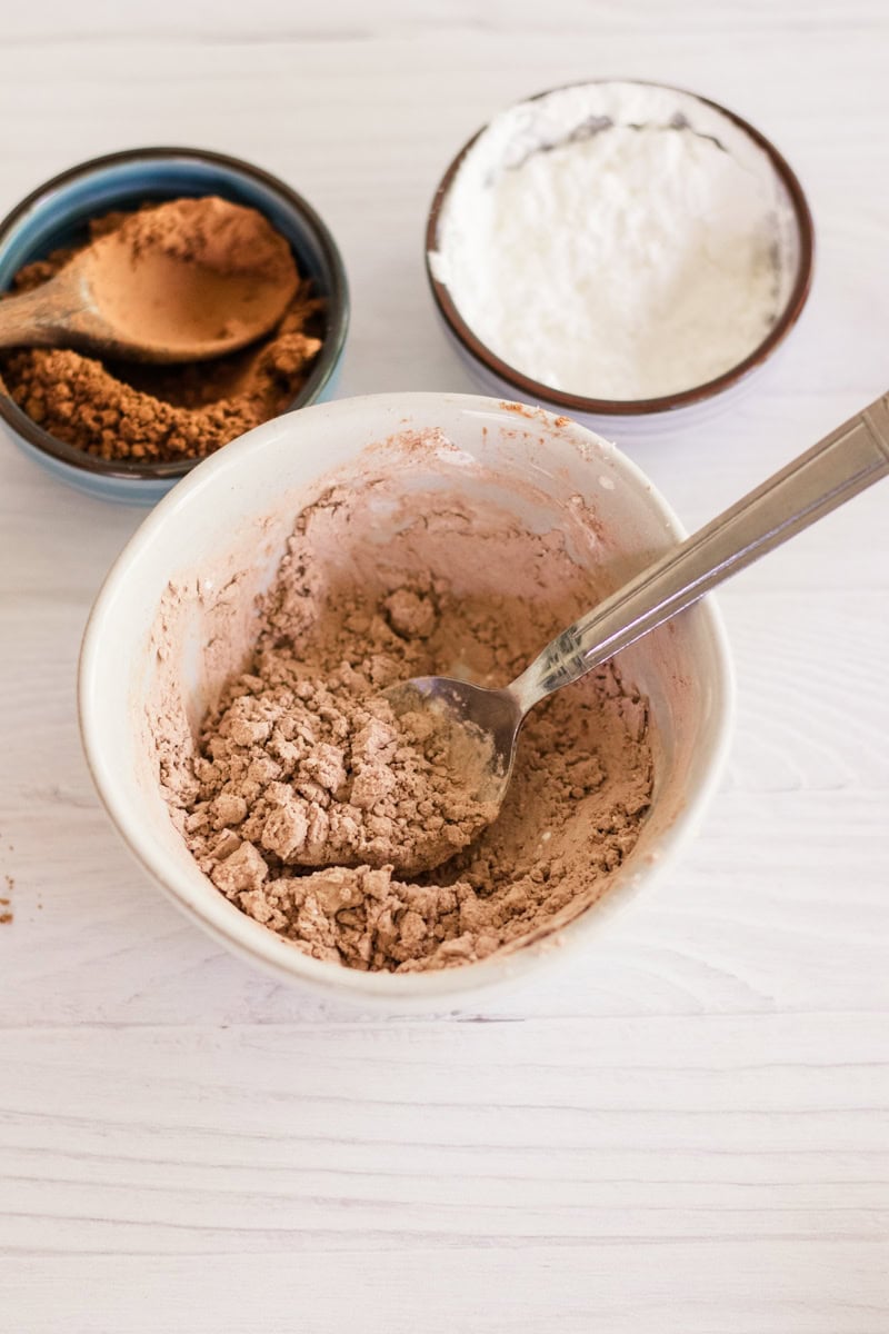 Dry shampoo mixed in a bowl with extra bowls of arrowroot powder and cocoa powder next to it. 
