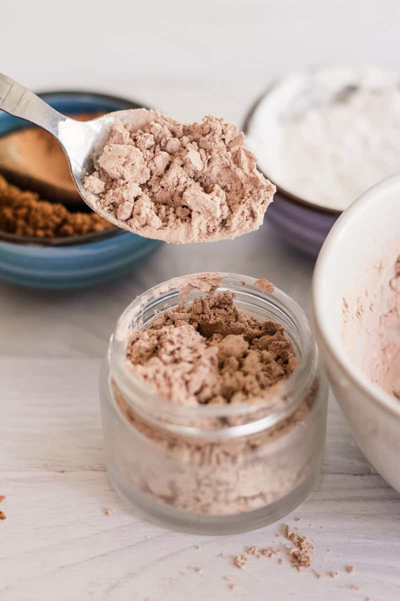 Spooning dry shampoo into a glass jar for storage. 