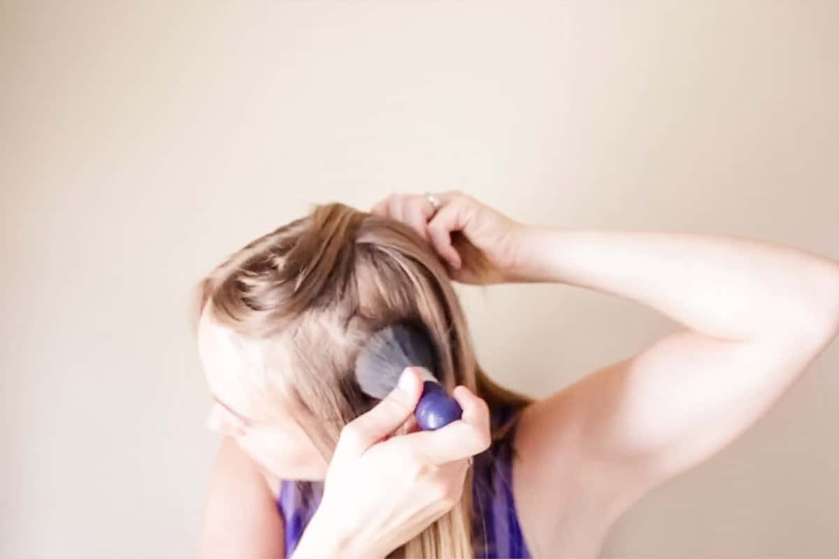 Applying dry shampoo to the scalp using a fluffy makeup brush.